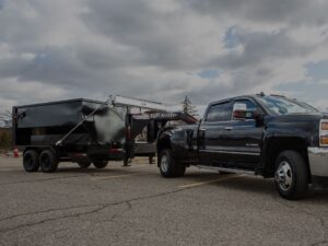 A black truck pulling a trailer with a large dump truck.